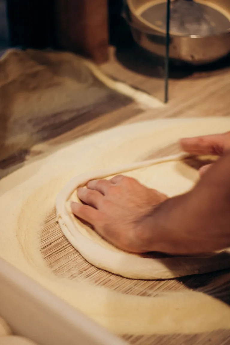 Mãos abrindo o disco de massa na semolina, luz quente