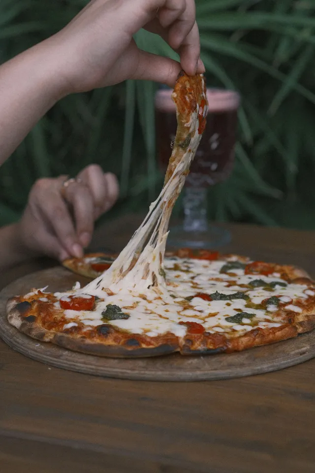 Fatia de pizza napolitana sendo puxada, com queijo derretido