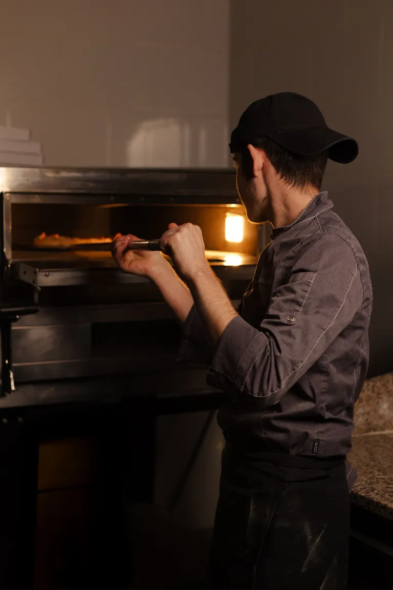 Pizzaiolo levando a pizza ao forno com a pá